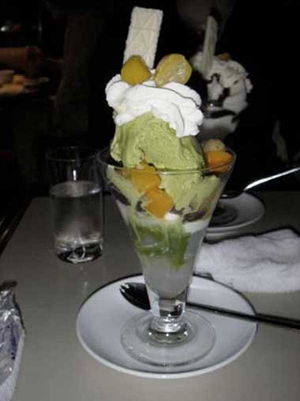 green ice cream with whipped cream and other unidentified fruit in a tall glass
