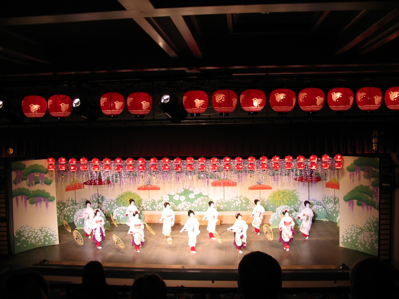 stage with geishas in white dresses lined with red lanterns
