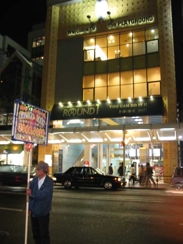 man holding a sign that says 'excite lady' outside of an arcade at night