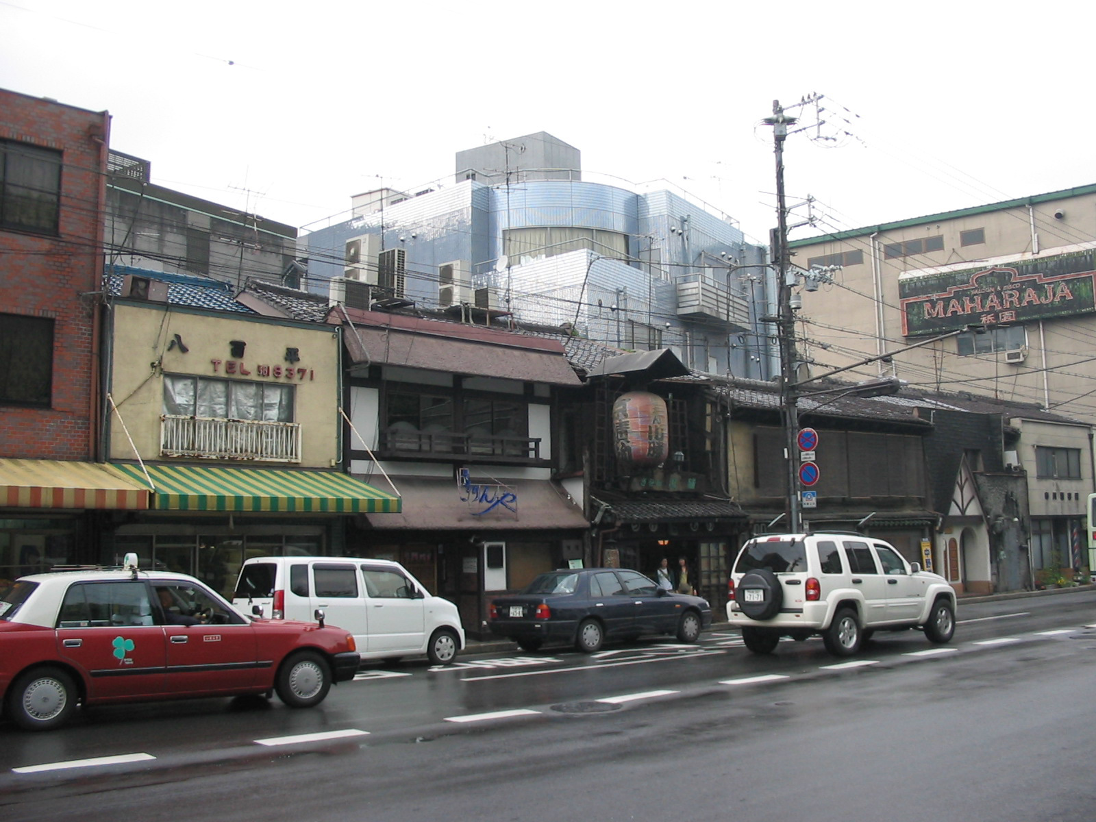 traffic in street in front of rundown short buildings with many electricity wires