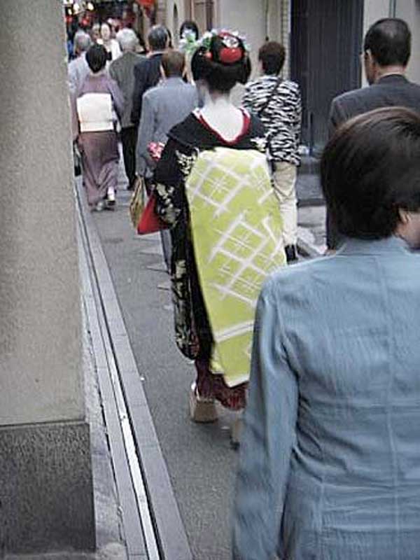 maiko walking down narrow street surrounded by people