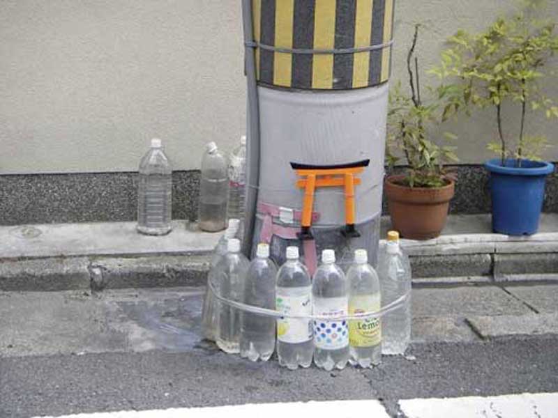 water bottles of water wrapped around a pole with a small orange torri gate on top