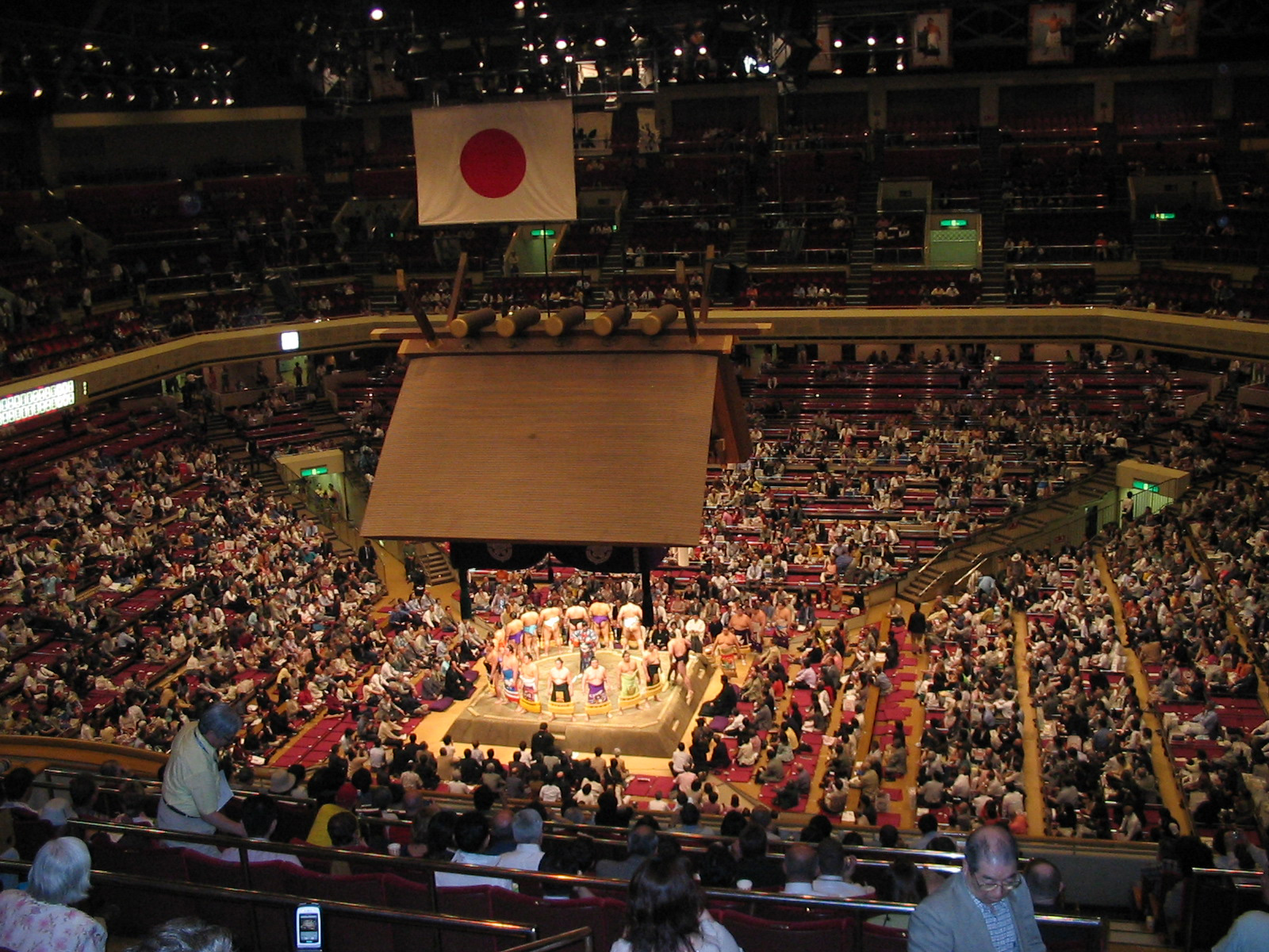 view from stands looking at men standing around circle with Japanese flag in background
